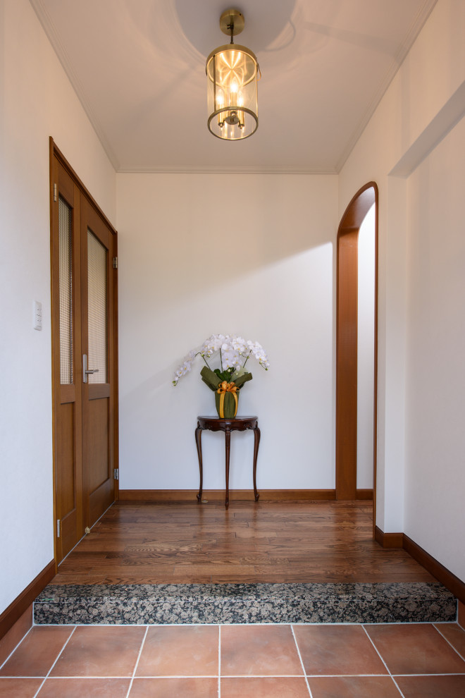 Источник вдохновения для домашнего уюта: узкая прихожая среднего размера в скандинавском стиле с белыми стенами, темным паркетным полом, поворотной входной дверью, коричневой входной дверью и коричневым полом