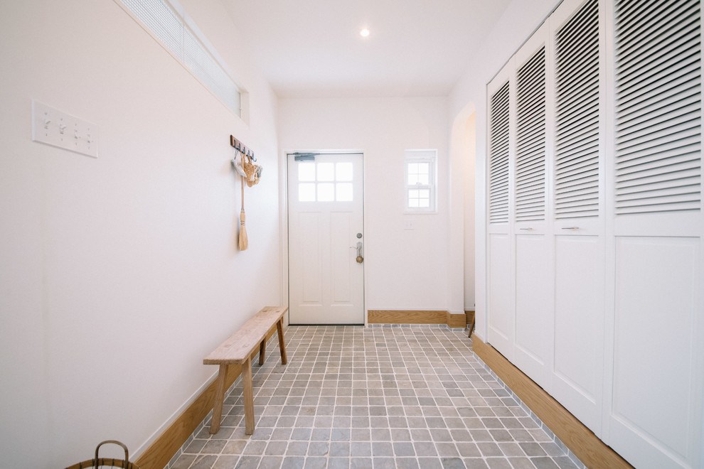 他の地域にあるトラディショナルスタイルのおしゃれな玄関ホール (白い壁、磁器タイルの床、白いドア、グレーの床) の写真