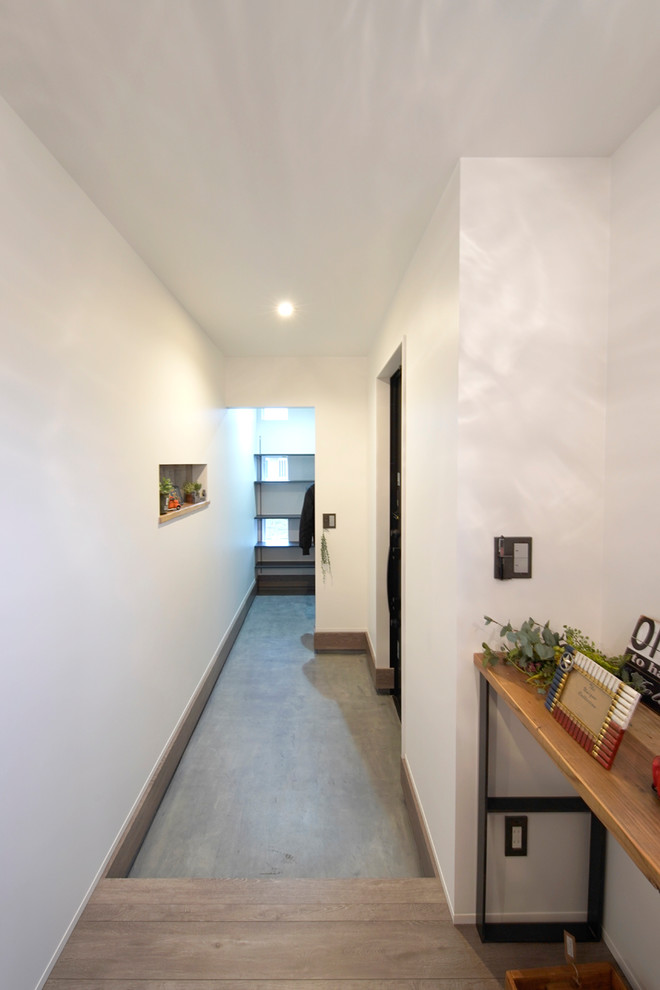 Foto di un corridoio industriale con pareti bianche, pavimento in cemento, una porta singola, una porta in legno scuro e pavimento grigio