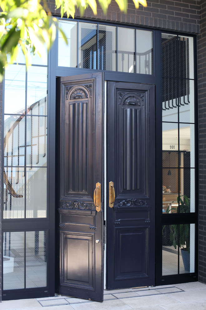 Klassisk inredning av en entré, med klinkergolv i terrakotta, en dubbeldörr och en svart dörr