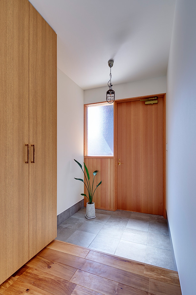 Ejemplo de entrada actual con paredes blancas, suelo de cemento, puerta simple, puerta de madera en tonos medios y suelo gris
