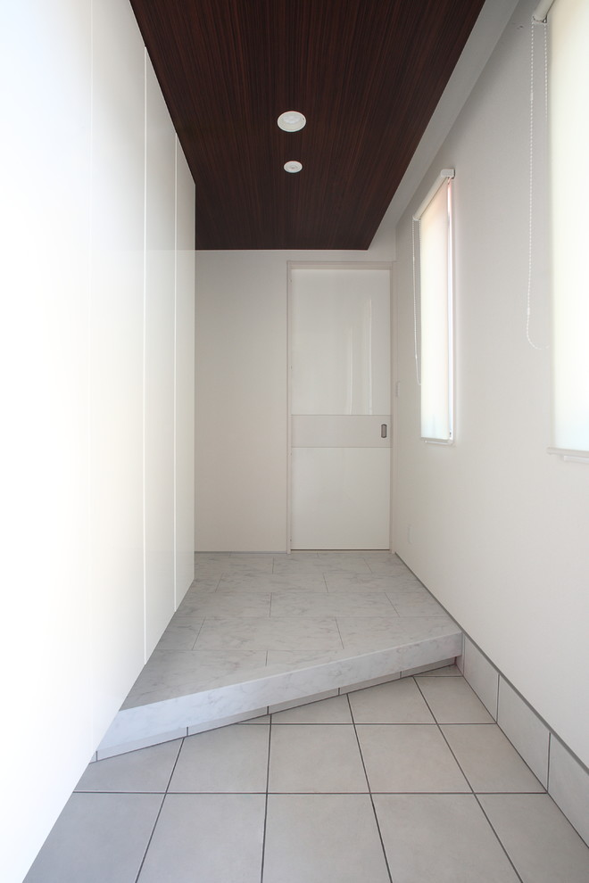 Réalisation d'une entrée design avec un mur blanc, un sol gris et un couloir.