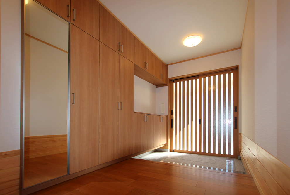 Modelo de hall minimalista pequeño con paredes blancas, suelo de contrachapado, puerta corredera, puerta de madera en tonos medios y suelo marrón