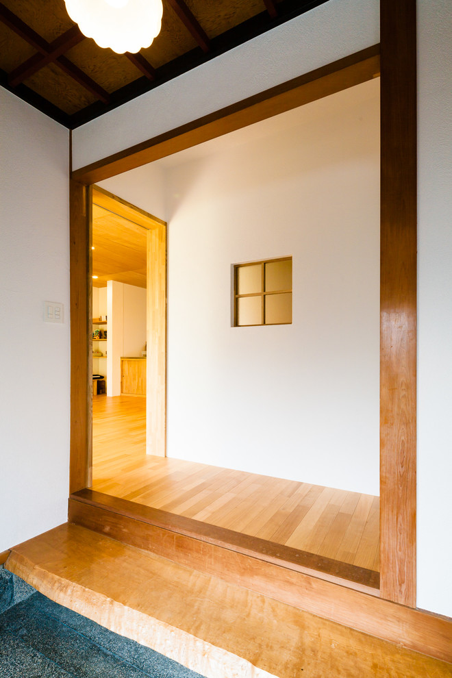Example of a small danish medium tone wood floor entryway design in Kyoto with white walls and a dark wood front door