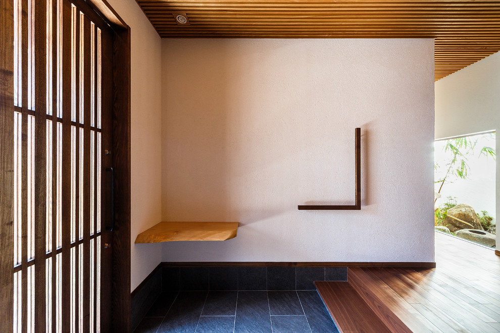 На фото: прихожая в восточном стиле с белыми стенами, темным паркетным полом, раздвижной входной дверью и коричневой входной дверью