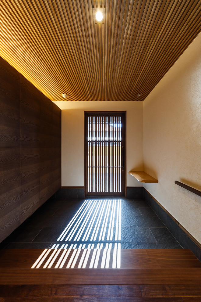 Réalisation d'une entrée asiatique avec un mur blanc, parquet foncé, une porte coulissante, une porte marron et un sol noir.