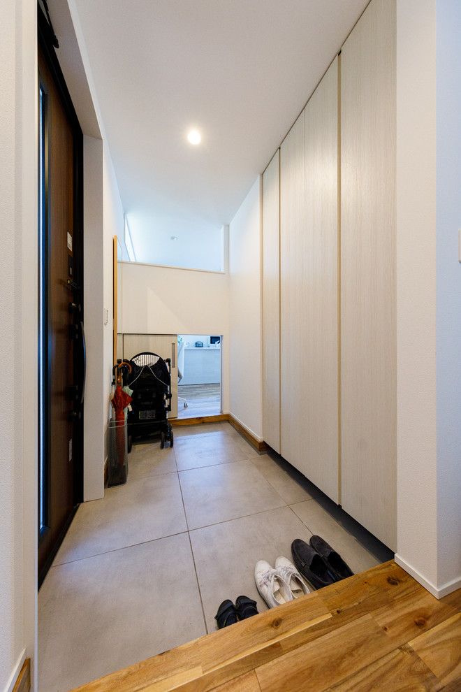 На фото: тамбур среднего размера в скандинавском стиле с белыми стенами, полом из керамогранита, одностворчатой входной дверью, коричневой входной дверью и серым полом