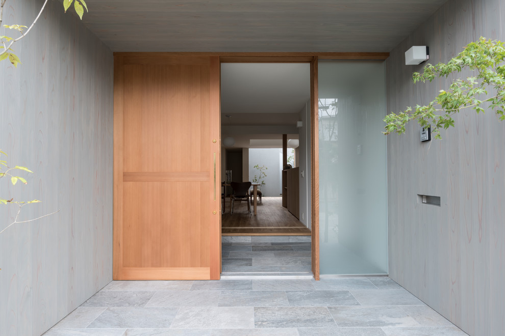 Idee per una porta d'ingresso moderna con pareti grigie, pavimento in pietra calcarea, una porta scorrevole e una porta in legno chiaro