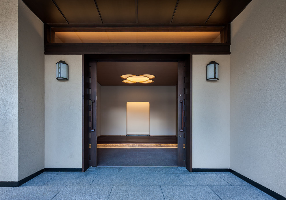 Cette image montre une entrée asiatique avec un couloir, un mur beige, sol en granite, une porte double, une porte en bois foncé et un sol gris.