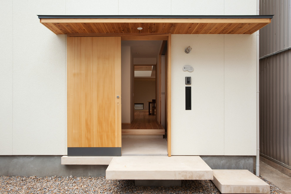 Cette image montre une porte d'entrée asiatique avec un mur blanc, sol en béton ciré, une porte coulissante et une porte en bois clair.