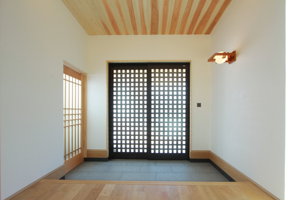 Cette image montre une entrée asiatique avec un mur blanc, un sol en bois brun, une porte noire et un sol beige.