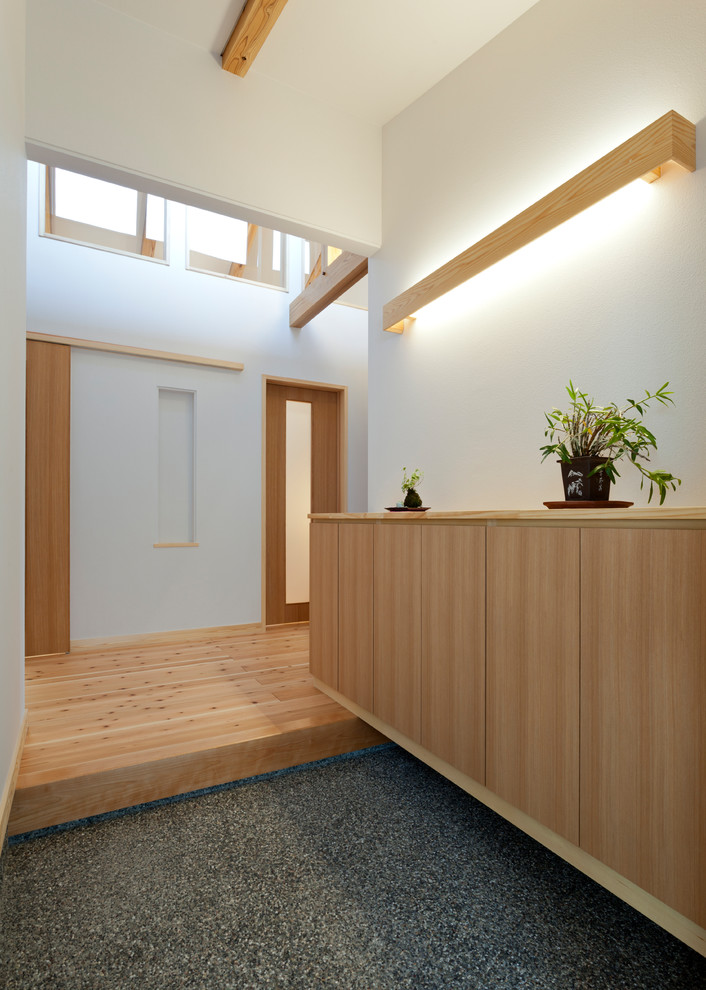 На фото: маленькая узкая прихожая в восточном стиле с белыми стенами, светлым паркетным полом, раздвижной входной дверью, входной дверью из светлого дерева и бежевым полом для на участке и в саду