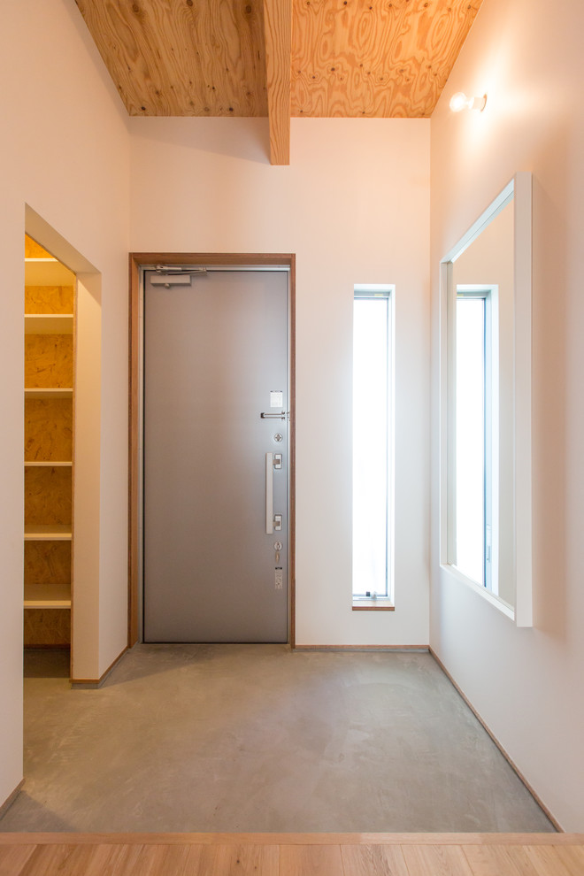 Modelo de puerta principal minimalista pequeña con paredes blancas, suelo de cemento, puerta simple, puerta metalizada y suelo gris