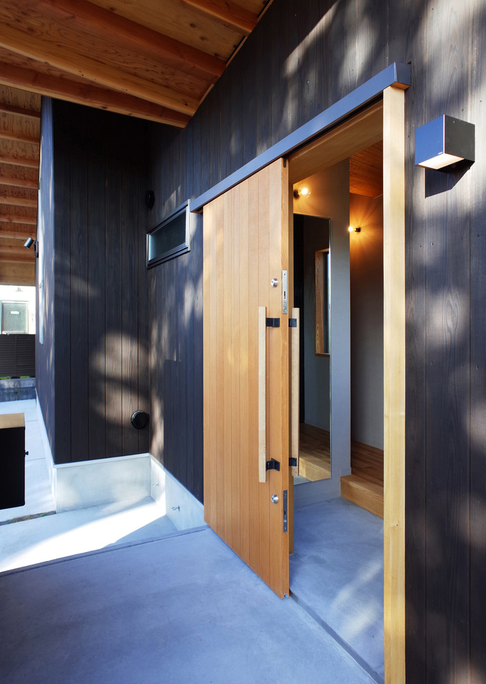 Idées déco pour une porte d'entrée scandinave de taille moyenne avec un mur noir, sol en béton ciré, une porte coulissante, une porte en bois brun et un sol gris.
