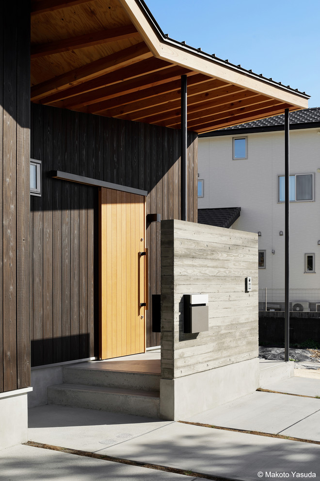 Idée de décoration pour une porte d'entrée nordique de taille moyenne avec un mur noir, sol en béton ciré, une porte coulissante, une porte en bois brun et un sol gris.