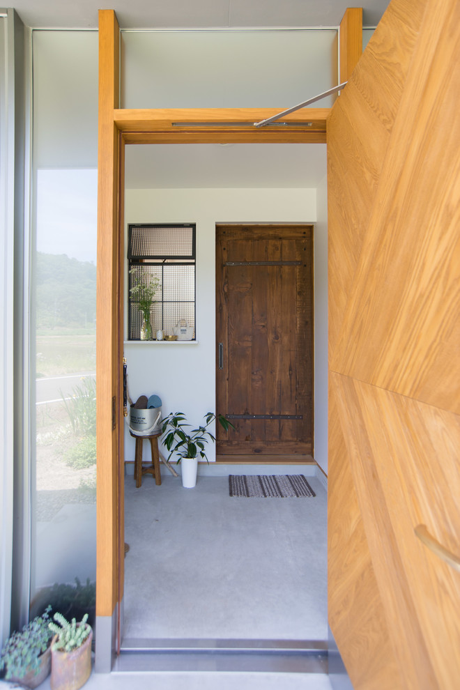На фото: узкая прихожая среднего размера в стиле кантри с белыми стенами, бетонным полом, одностворчатой входной дверью, входной дверью из дерева среднего тона и серым полом
