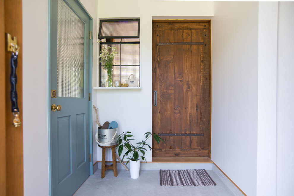 Ispirazione per un corridoio stile shabby di medie dimensioni con pareti bianche, pavimento in cemento, pavimento grigio, una porta singola e una porta in legno bruno