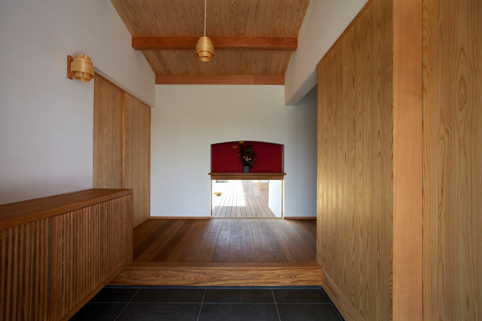 Asiatischer Eingang mit Korridor, weißer Wandfarbe, Schiebetür, braunem Holzboden, heller Holzhaustür und beigem Boden in Sonstige