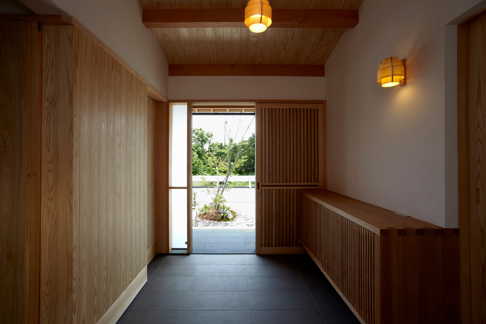Modelo de hall asiático con paredes blancas, puerta corredera, suelo de madera en tonos medios, puerta de madera clara y suelo beige