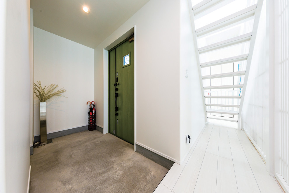 Modern inredning av en mellanstor foajé, med vita väggar, betonggolv, en enkeldörr, en grön dörr och grått golv