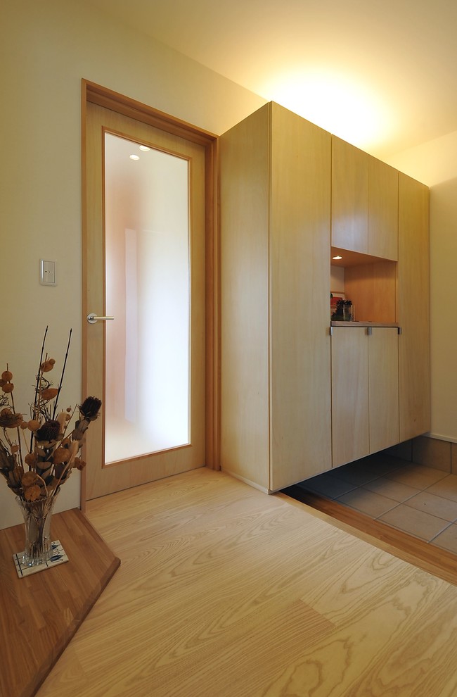 Modern inredning av en mellanstor foajé, med vita väggar, plywoodgolv, en enkeldörr, en brun dörr och beiget golv