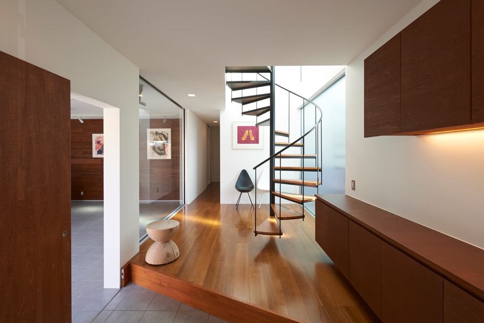 Aménagement d'une entrée contemporaine avec un mur blanc, un sol en bois brun et un couloir.