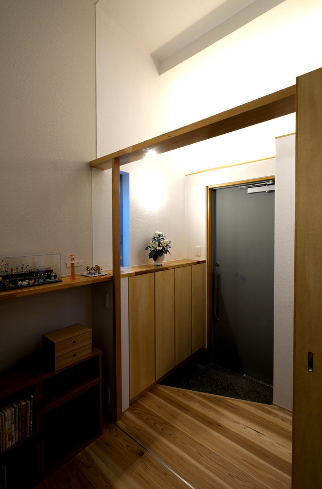 Inredning av en modern liten hall, med vita väggar, ljust trägolv, en enkeldörr, en grå dörr och beiget golv