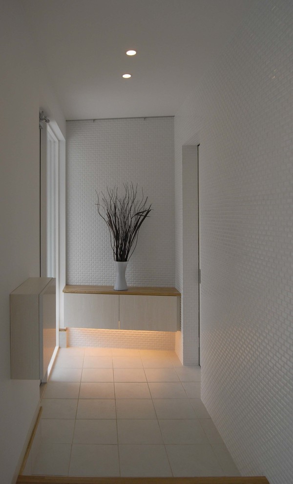 Modern inredning av en hall, med vita väggar, klinkergolv i keramik, en enkeldörr, ljus trädörr och vitt golv