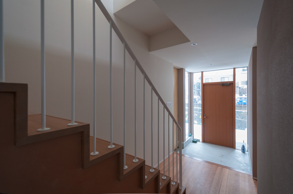Cette photo montre une entrée moderne avec un couloir, un mur blanc, un sol en contreplaqué et une porte en bois brun.