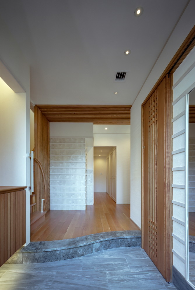 Foto på en orientalisk hall, med vita väggar, klinkergolv i porslin, mellanmörk trädörr och grått golv