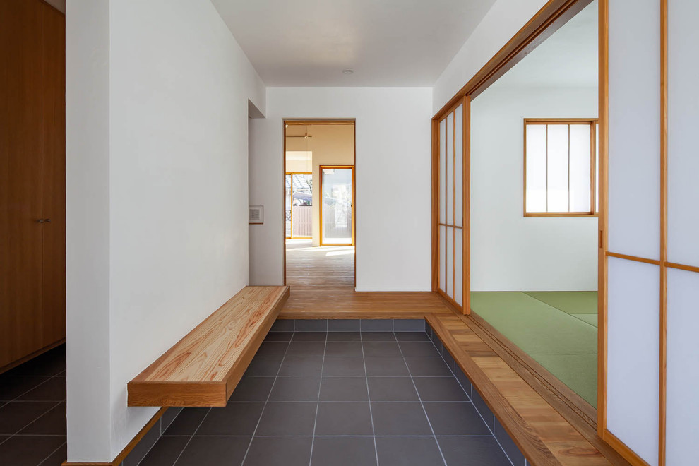 Kleiner Asiatischer Eingang mit Korridor, weißer Wandfarbe, braunem Holzboden, Schiebetür, hellbrauner Holzhaustür und beigem Boden in Sonstige