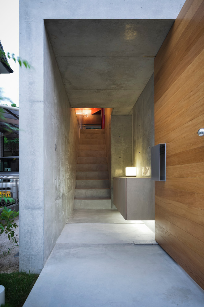 Réalisation d'une entrée minimaliste de taille moyenne avec un couloir, un mur gris, sol en béton ciré, une porte simple et une porte en bois brun.