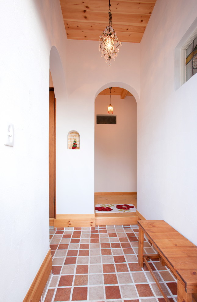 Exempel på en asiatisk entré, med vita väggar, klinkergolv i terrakotta och brunt golv