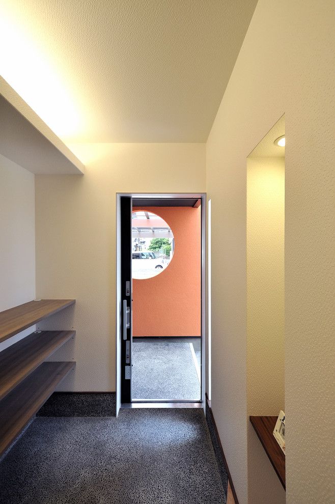 Réalisation d'une entrée minimaliste avec un couloir, un mur blanc, un sol en terrazzo, une porte coulissante, une porte en bois foncé et un sol noir.