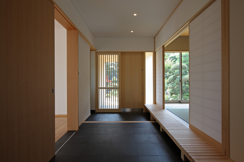 Cette photo montre un grand hall d'entrée asiatique avec un mur blanc, une porte coulissante, une porte en bois clair et un sol noir.