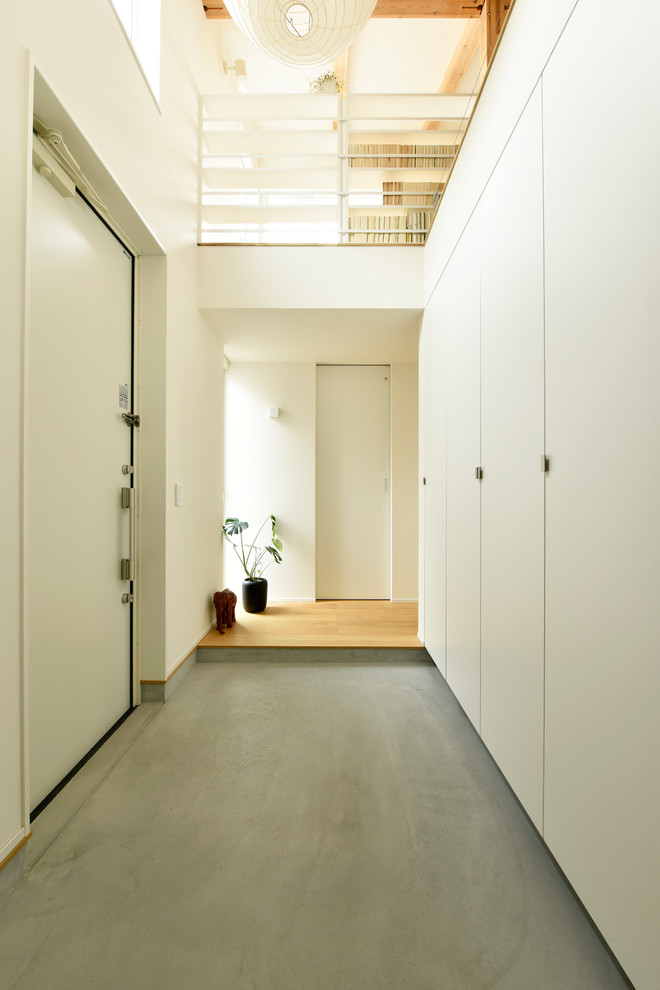 Свежая идея для дизайна: узкая прихожая в стиле модернизм с белыми стенами, бетонным полом, одностворчатой входной дверью, белой входной дверью и серым полом - отличное фото интерьера