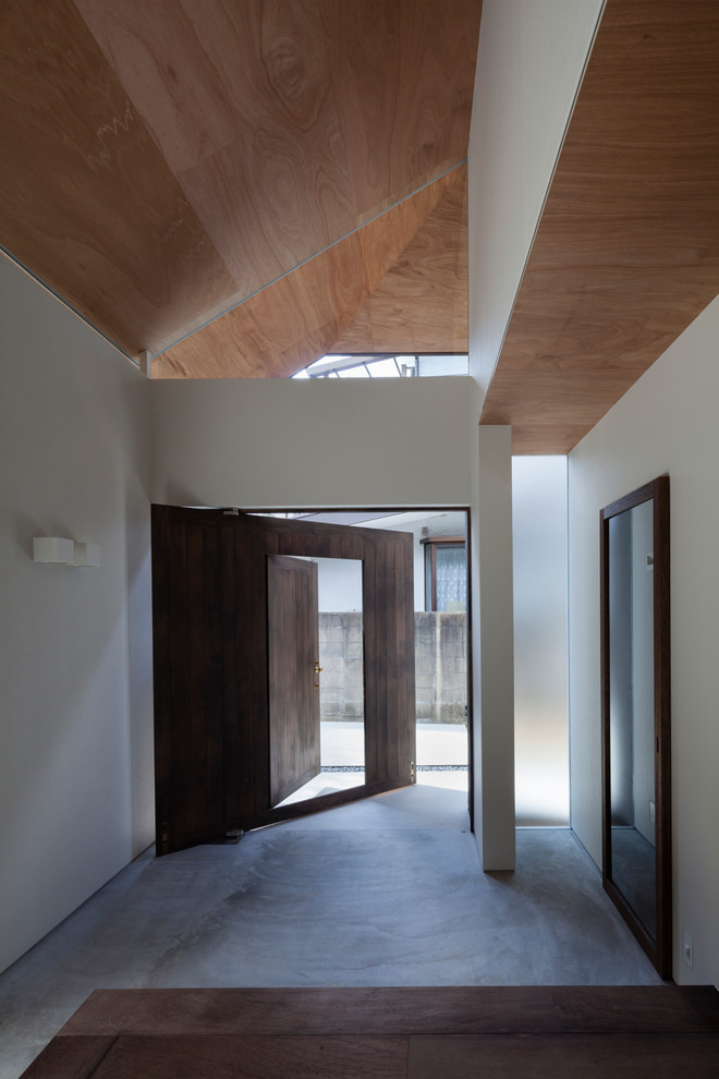 Réalisation d'une petite entrée minimaliste avec un couloir, un mur blanc, sol en béton ciré, une porte simple, une porte en bois foncé et un sol gris.