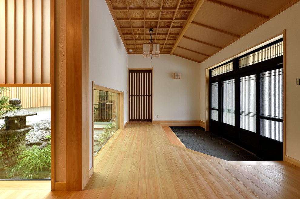 Inspiration för stora asiatiska hallar, med vita väggar, ljust trägolv, en skjutdörr, en svart dörr och brunt golv