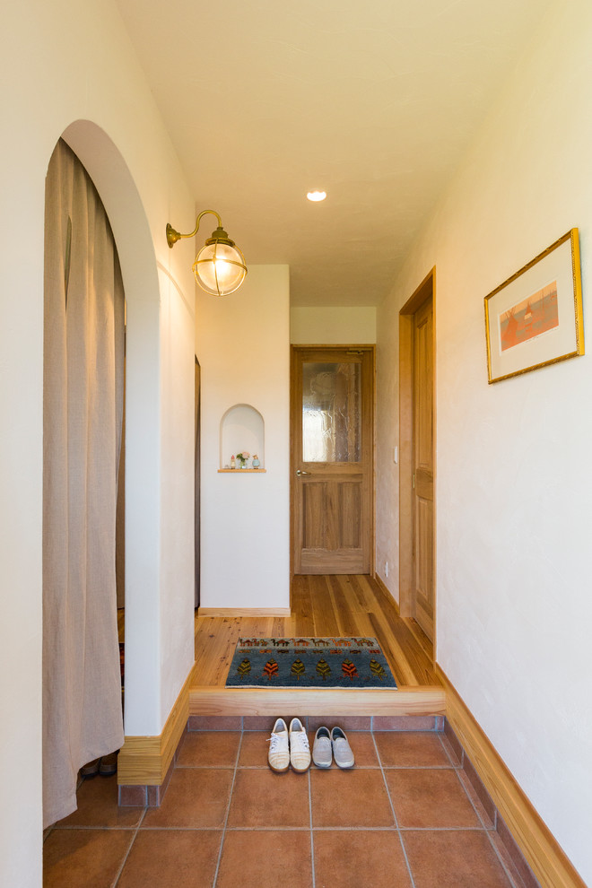 Aménagement d'une entrée montagne avec un couloir, un mur blanc, tomettes au sol et un sol marron.