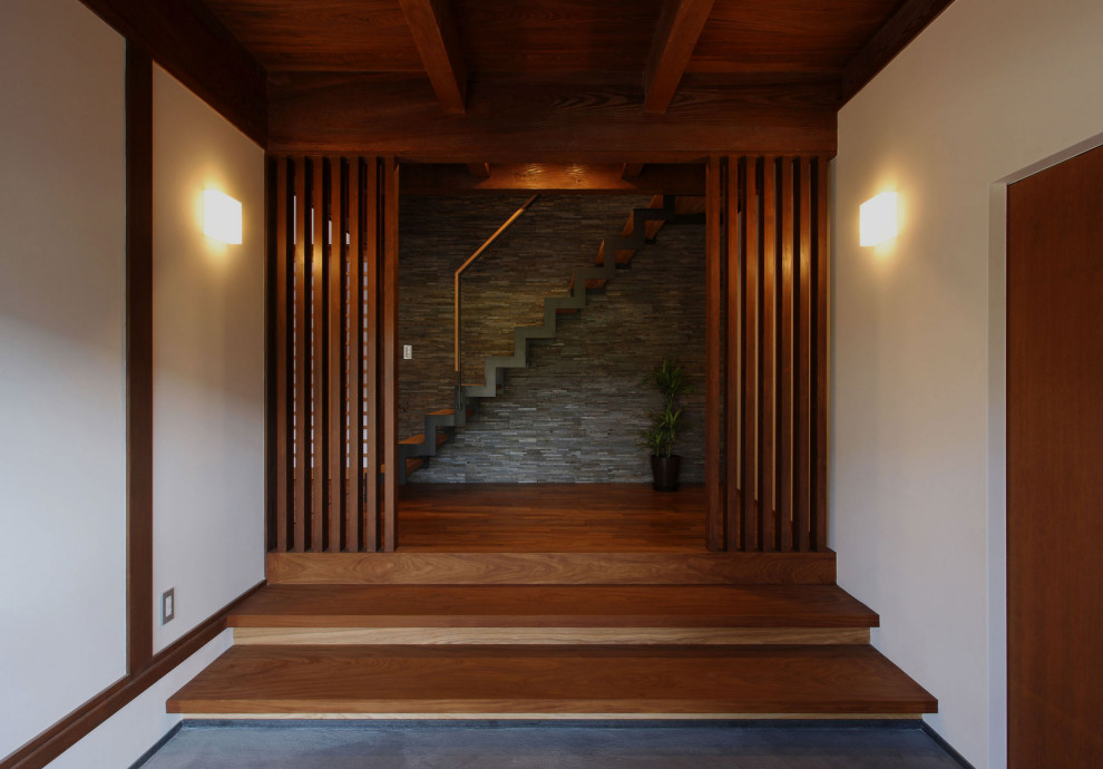 Стильный дизайн: узкая прихожая среднего размера в восточном стиле с белыми стенами, бетонным полом, раздвижной входной дверью, коричневой входной дверью и серым полом - последний тренд