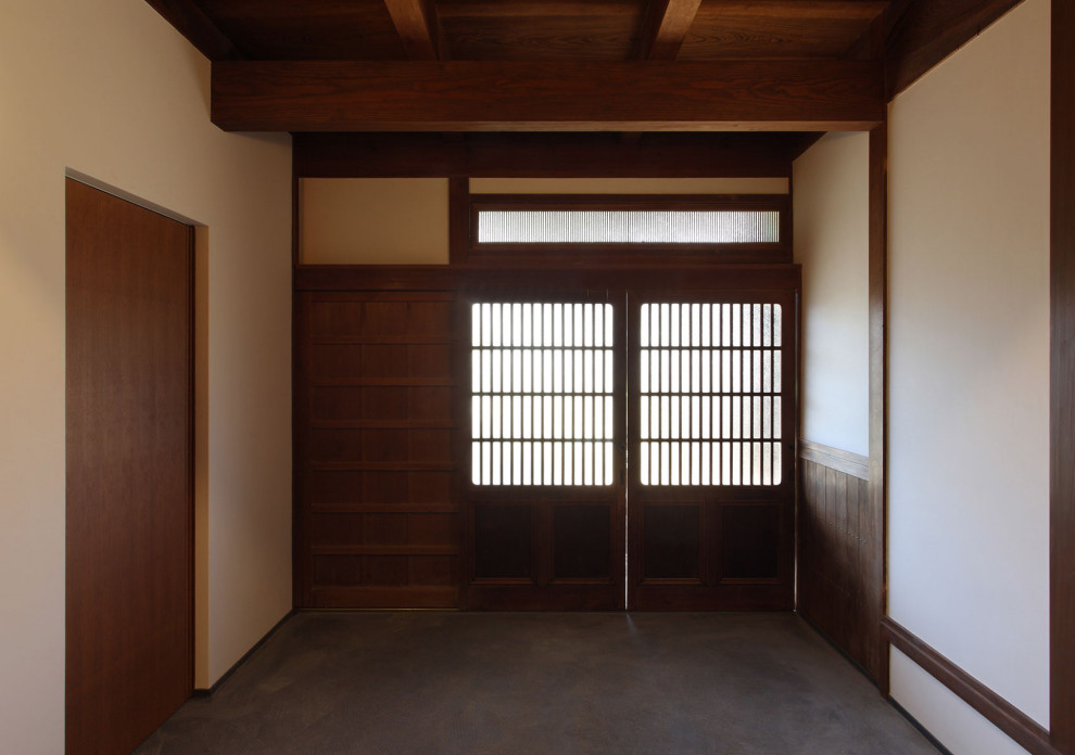 Asiatisk inredning av en mellanstor hall, med vita väggar, betonggolv, en skjutdörr, en brun dörr och grått golv