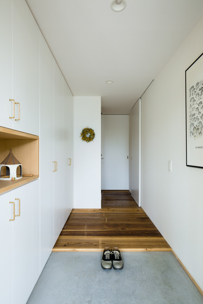 Cette image montre une entrée minimaliste avec un couloir, un mur blanc, sol en béton ciré et un sol gris.
