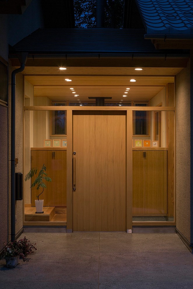 Modelo de puerta principal asiática con paredes beige, suelo de cemento, puerta simple y puerta de madera clara