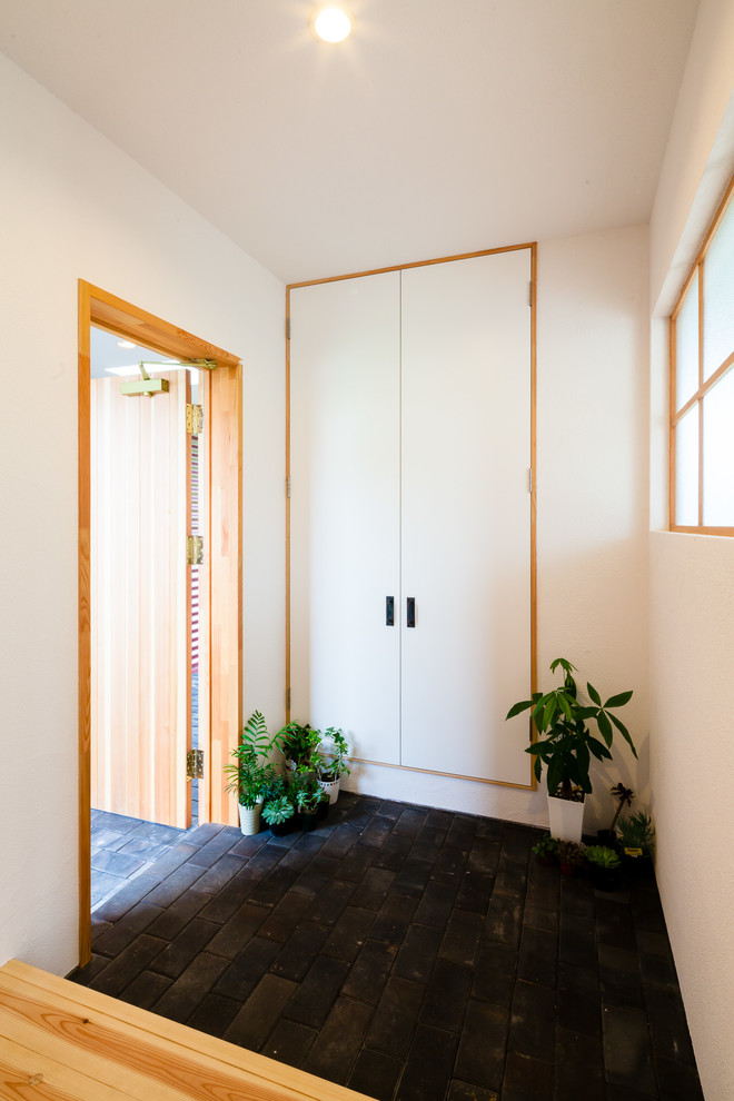 Imagen de hall asiático de tamaño medio con paredes blancas, suelo de ladrillo, puerta simple, puerta de madera en tonos medios y suelo negro