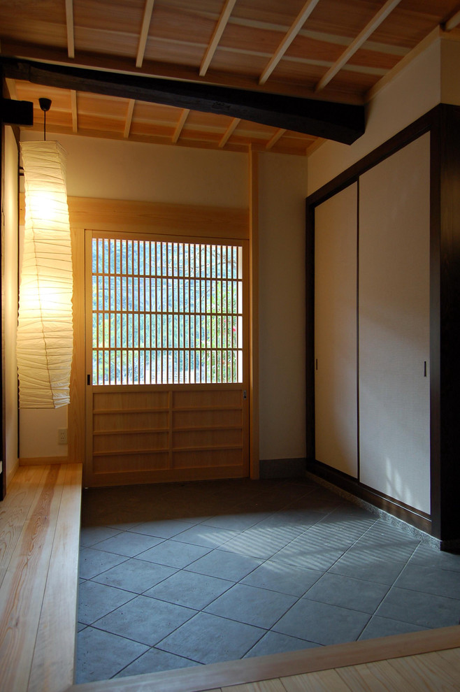 Asiatischer Eingang mit weißer Wandfarbe, Porzellan-Bodenfliesen, Schiebetür, heller Holzhaustür und grauem Boden in Sonstige