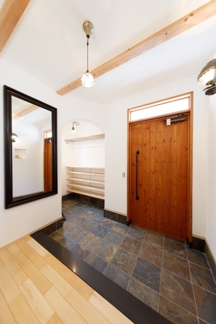 На фото: узкая прихожая в восточном стиле с белыми стенами, полом из сланца, одностворчатой входной дверью и входной дверью из дерева среднего тона