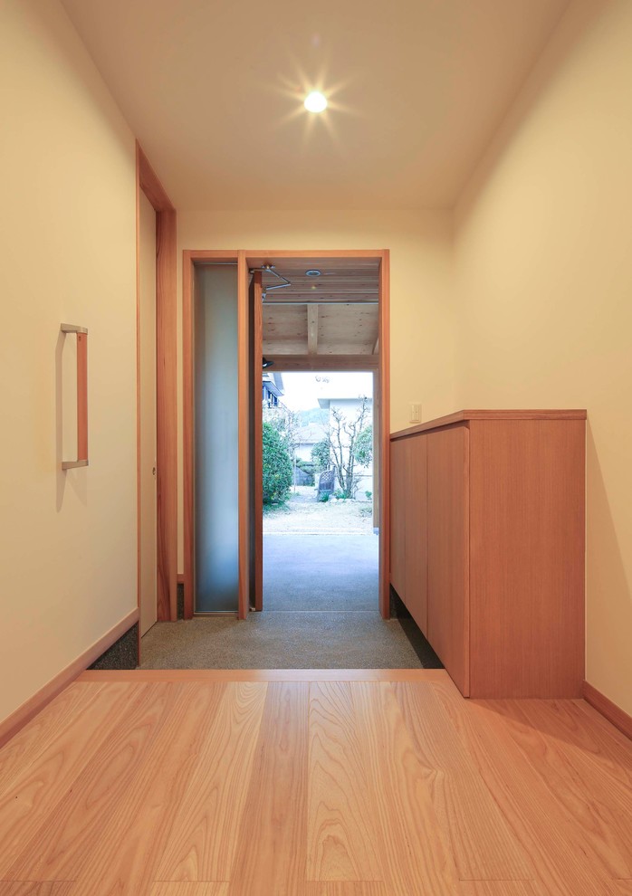 Aménagement d'une entrée asiatique avec un mur blanc, une porte simple et une porte en bois brun.