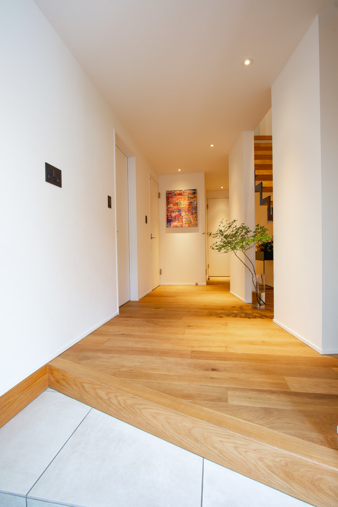 Cette image montre une entrée asiatique avec un mur blanc, un sol en bois brun et un couloir.