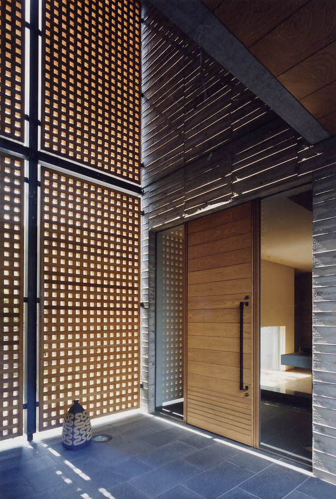 Asiatische Haustür mit Drehtür, hellbrauner Holzhaustür, grauer Wandfarbe und grauem Boden in Yokohama