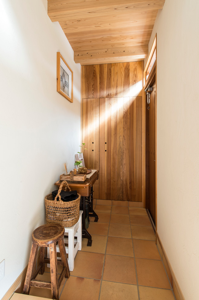 Cette image montre une petite entrée asiatique avec un couloir, un mur blanc, une porte en bois brun et tomettes au sol.